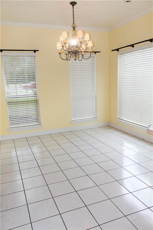 unfurnished dining area with an inviting chandelier, light tile patterned floors, plenty of natural light, and ornamental molding