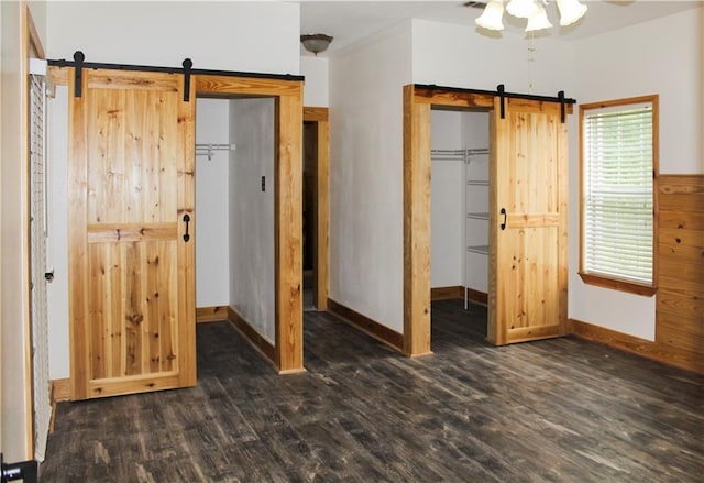 unfurnished bedroom with ceiling fan, a barn door, dark hardwood / wood-style flooring, and a closet