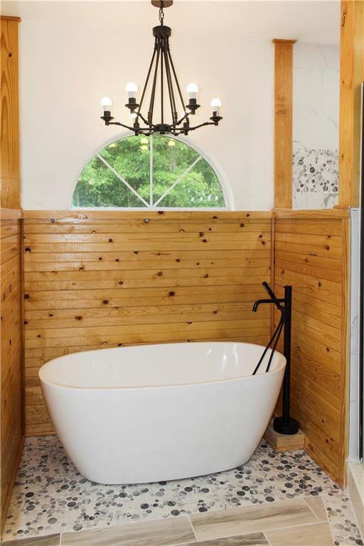 bathroom with plenty of natural light, a bath, a notable chandelier, and tile patterned floors