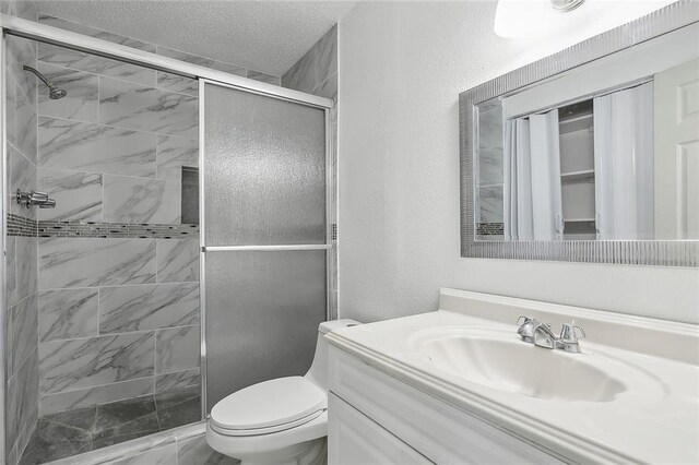 bathroom with a textured ceiling, toilet, vanity, and an enclosed shower