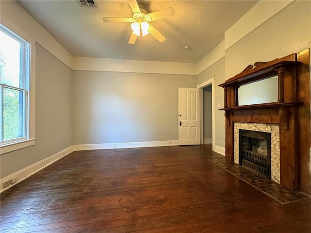 unfurnished living room with a healthy amount of sunlight, a stone fireplace, dark hardwood / wood-style floors, and ceiling fan