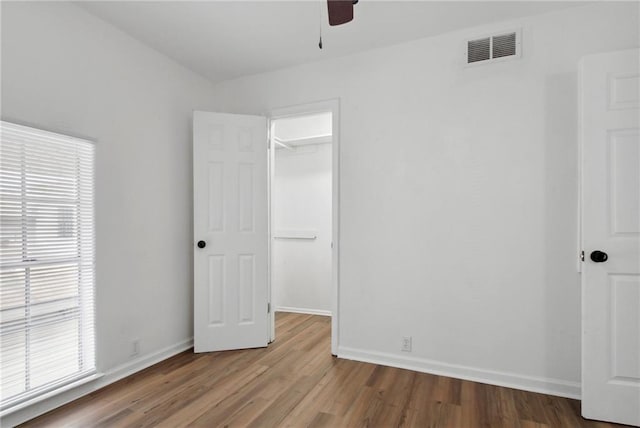 unfurnished bedroom featuring a walk in closet, wood-type flooring, a closet, and ceiling fan