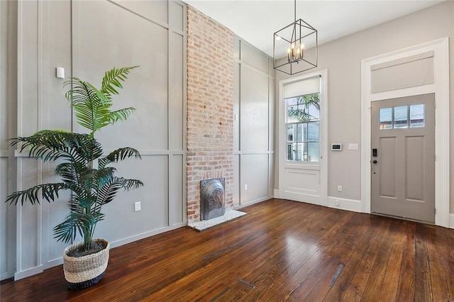 foyer entrance featuring a notable chandelier, a brick fireplace, and dark hardwood / wood-style flooring