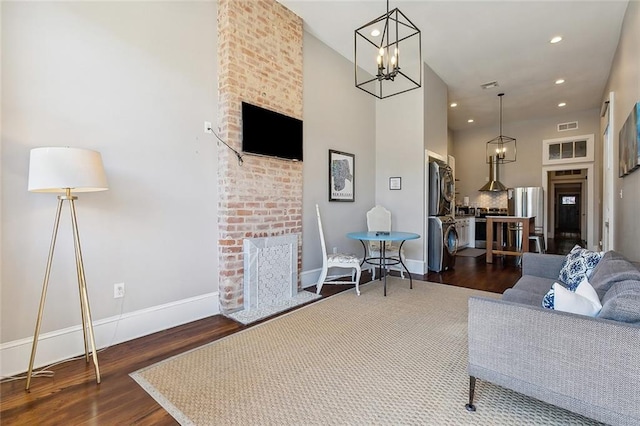 living room featuring a brick fireplace, stacked washer and clothes dryer, and dark hardwood / wood-style flooring