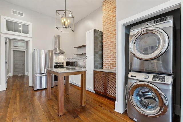 kitchen featuring white cabinetry, decorative backsplash, stacked washer / drying machine, stainless steel appliances, and wall chimney exhaust hood