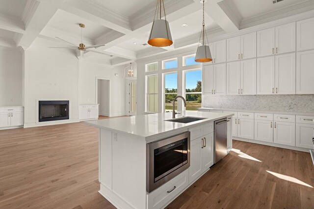 kitchen with appliances with stainless steel finishes, sink, a fireplace, white cabinets, and a center island with sink