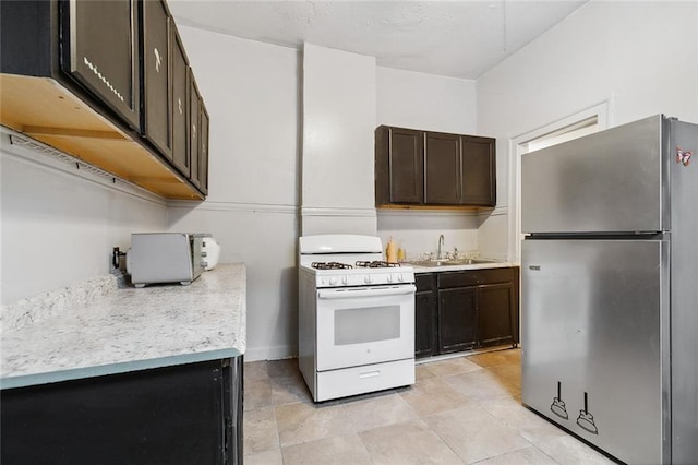 kitchen with dark brown cabinets, sink, white range with gas cooktop, stainless steel refrigerator, and light tile patterned floors