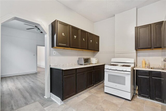 kitchen with white range with gas cooktop, ceiling fan, light wood-type flooring, and dark brown cabinetry