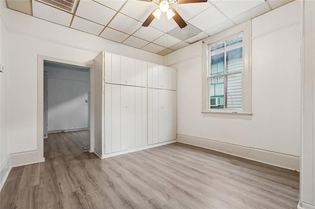 unfurnished bedroom featuring ceiling fan, light wood-type flooring, and a drop ceiling