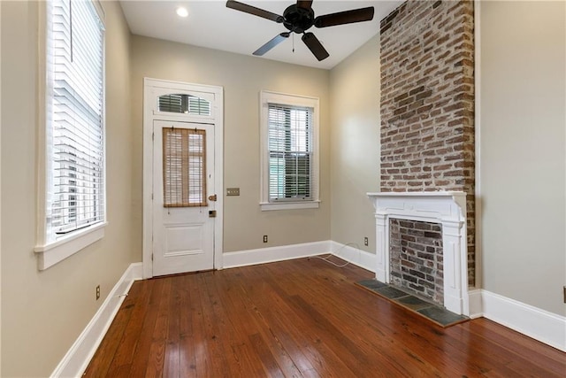 entryway with a brick fireplace, dark wood-type flooring, and ceiling fan