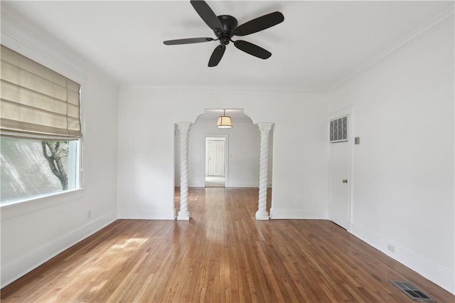 empty room with decorative columns, crown molding, ceiling fan, and wood-type flooring