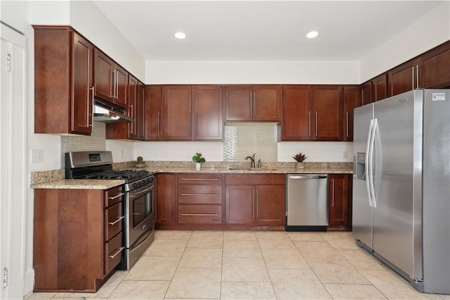 kitchen featuring tasteful backsplash, light stone countertops, appliances with stainless steel finishes, and sink