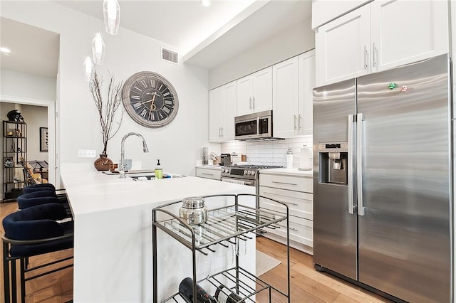 kitchen with backsplash, stainless steel appliances, light hardwood / wood-style floors, white cabinets, and a kitchen bar