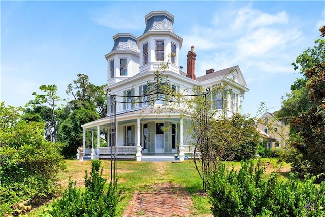 victorian home featuring a porch, a front yard, a balcony, and a chimney