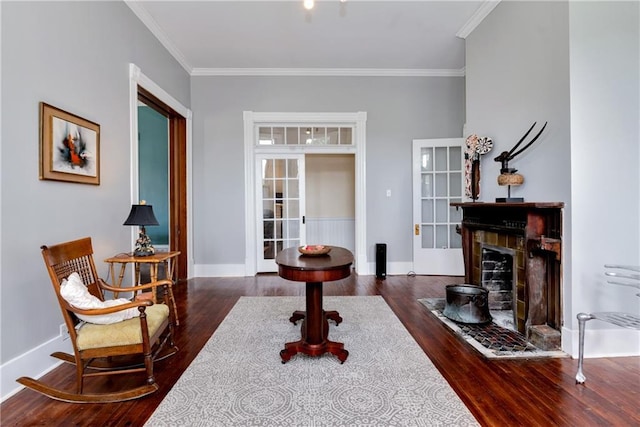 living area featuring baseboards, wood finished floors, a fireplace, and crown molding