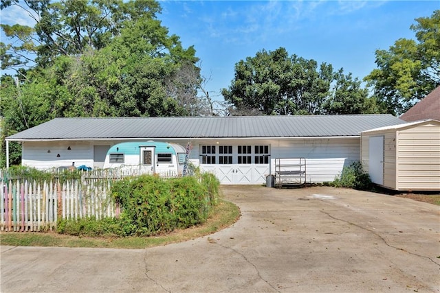 ranch-style house featuring driveway, an outbuilding, metal roof, and fence