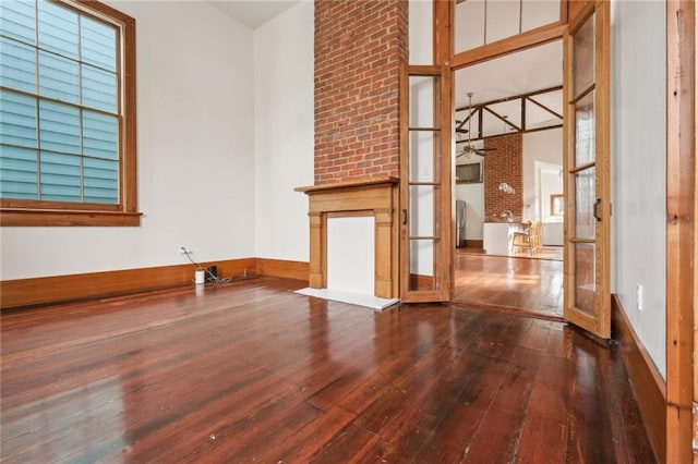 unfurnished room featuring dark wood-style floors, a large fireplace, and baseboards