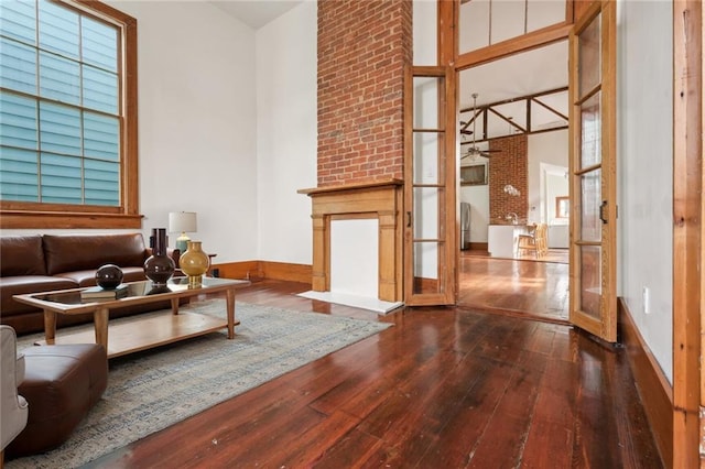 living area with baseboards, a large fireplace, a high ceiling, and hardwood / wood-style flooring