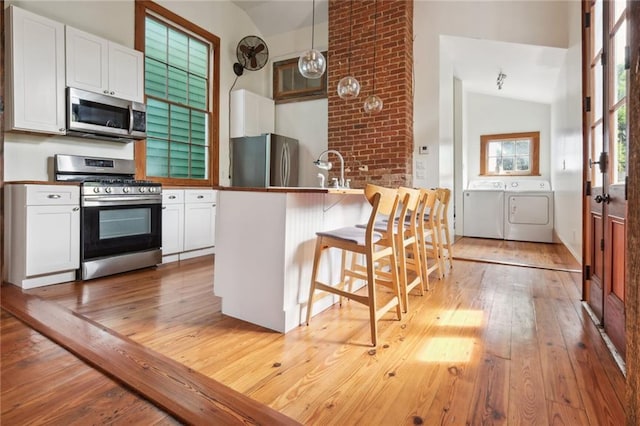 1915 Governor Nicholls St, New Orleans, LA 70116 - kitchen with appliances with stainless steel finishes, washing machine and clothes dryer, vaulted ceiling, light wood-style floors, and white cabinetry