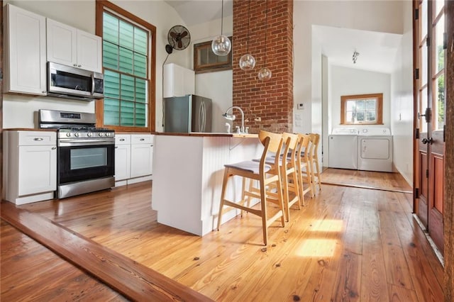 kitchen featuring pendant lighting, stainless steel appliances, white cabinetry, washer and dryer, and a kitchen breakfast bar