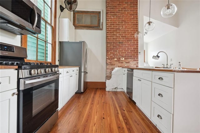 kitchen featuring hanging light fixtures, light wood-style flooring, appliances with stainless steel finishes, white cabinets, and brick wall