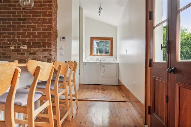 interior space featuring washer and clothes dryer, light wood-style flooring, vaulted ceiling, track lighting, and brick wall