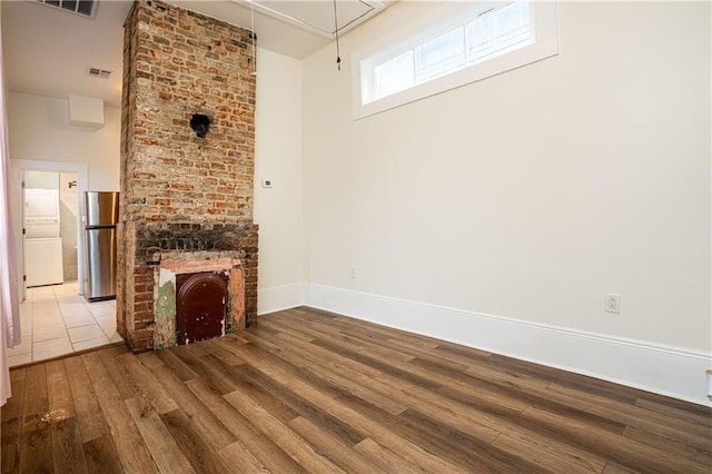 unfurnished living room featuring visible vents, a brick fireplace, baseboards, wood finished floors, and attic access
