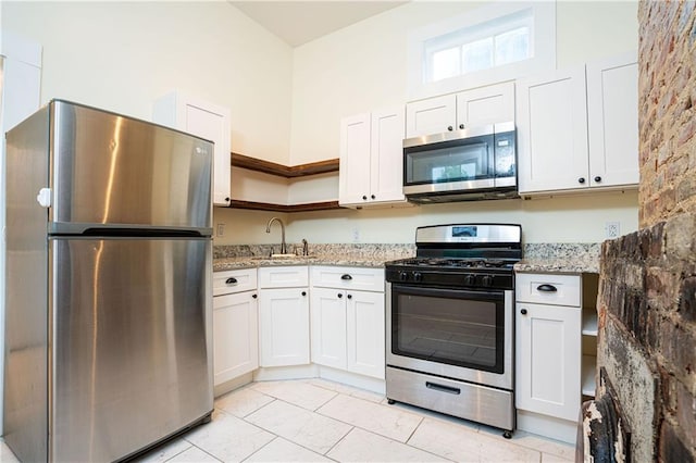 kitchen featuring a sink, open shelves, white cabinetry, light stone countertops, and appliances with stainless steel finishes
