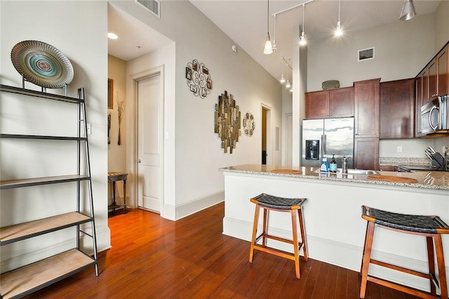 kitchen featuring stainless steel appliances, a kitchen breakfast bar, light stone counters, dark wood-style flooring, and a peninsula