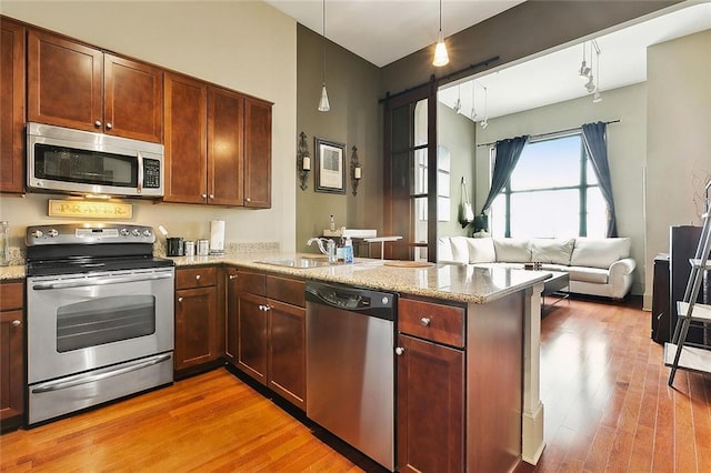 kitchen featuring appliances with stainless steel finishes, a peninsula, a sink, and light wood finished floors