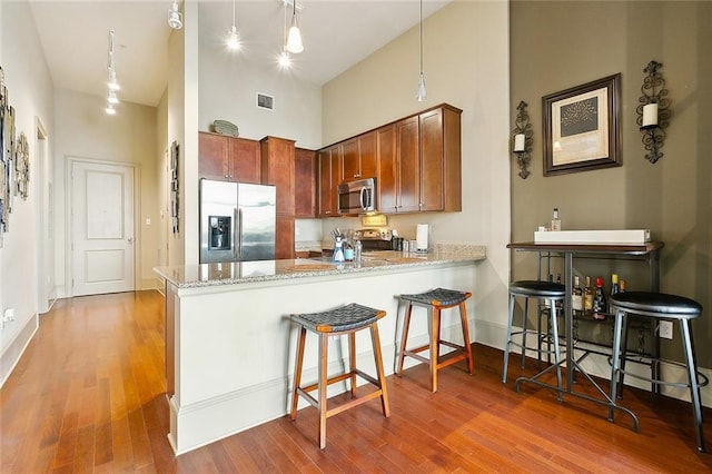 kitchen with appliances with stainless steel finishes, high vaulted ceiling, a peninsula, wood finished floors, and light stone counters