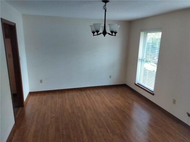 spare room featuring an inviting chandelier and dark wood-type flooring