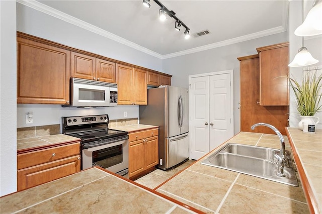 kitchen with appliances with stainless steel finishes, sink, tile countertops, and pendant lighting