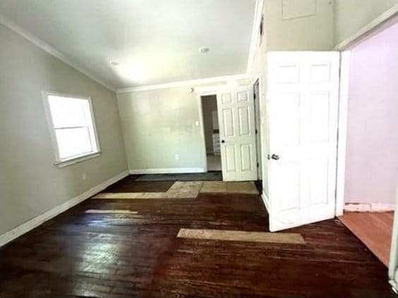 empty room featuring lofted ceiling, crown molding, and dark wood-type flooring