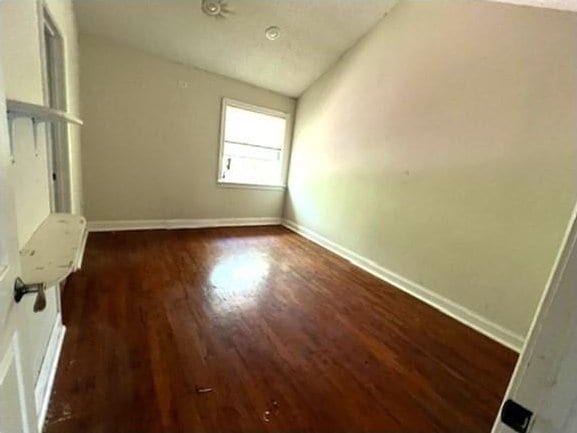 empty room with dark wood-type flooring and vaulted ceiling