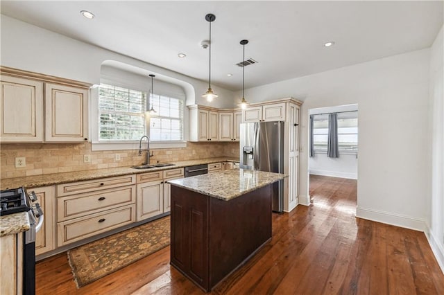 kitchen with light stone counters, dark hardwood / wood-style floors, sink, a kitchen island, and appliances with stainless steel finishes