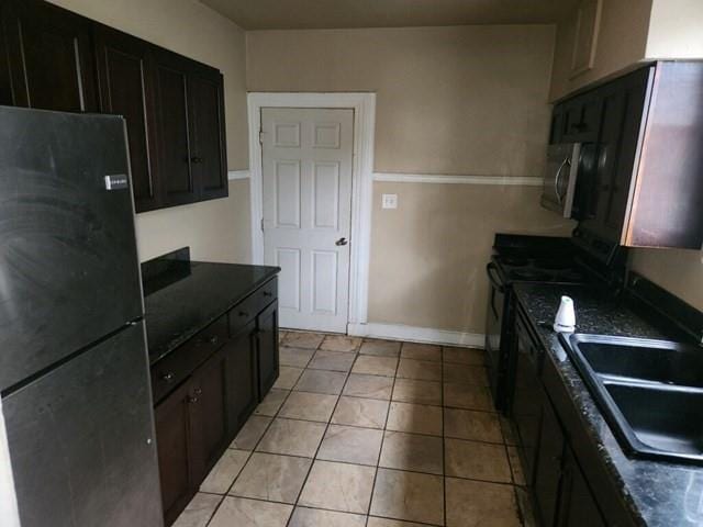 kitchen with light tile patterned floors, a sink, black appliances, dark brown cabinets, and baseboards