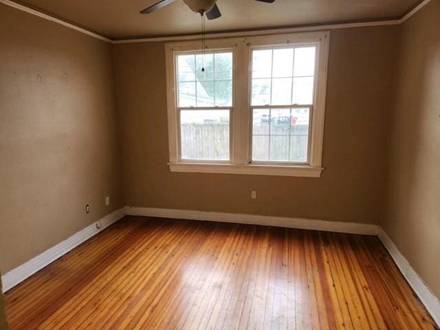 empty room featuring ornamental molding, light wood-type flooring, baseboards, and a ceiling fan