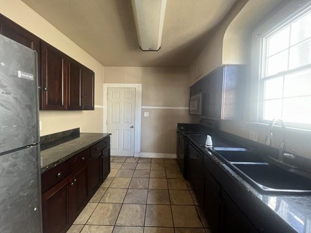 kitchen featuring baseboards, appliances with stainless steel finishes, a sink, and light tile patterned flooring