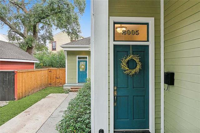 doorway to property with a shingled roof and fence