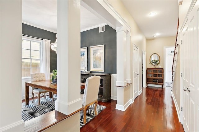 hallway with dark wood-style floors, visible vents, baseboards, and decorative columns