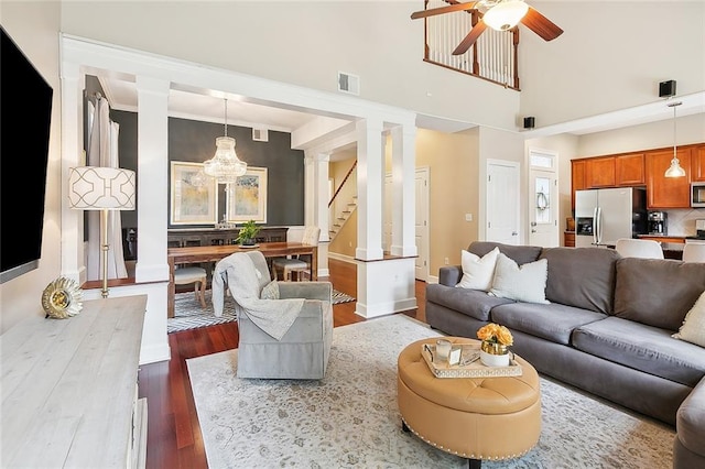 living room featuring ceiling fan with notable chandelier, wood-type flooring, ornate columns, and ornamental molding