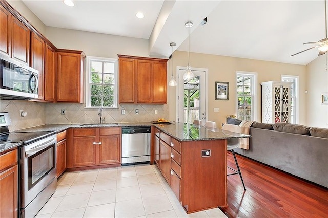 kitchen with ceiling fan, stainless steel appliances, plenty of natural light, light wood-type flooring, and a kitchen breakfast bar