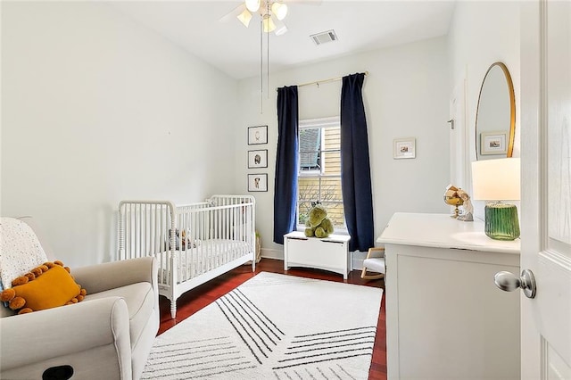 bedroom with a crib, dark wood-type flooring, and ceiling fan