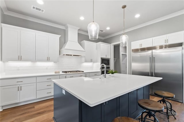 kitchen featuring a sink, built in appliances, visible vents, ornamental molding, and custom exhaust hood