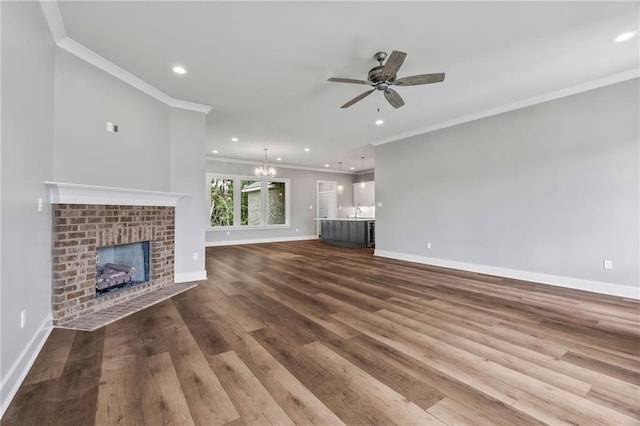 unfurnished living room featuring ceiling fan with notable chandelier, hardwood / wood-style floors, a fireplace, sink, and ornamental molding