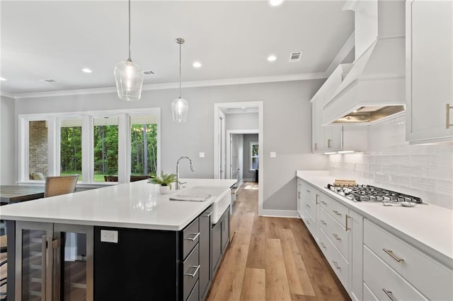 kitchen with stainless steel gas cooktop, a sink, custom range hood, tasteful backsplash, and light countertops