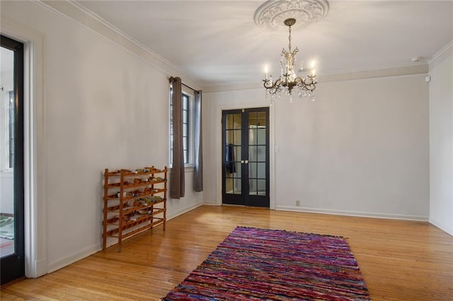 interior space featuring ornamental molding, an inviting chandelier, light wood-type flooring, and french doors