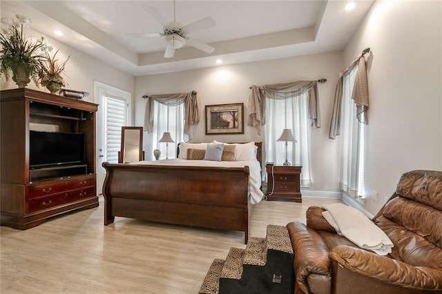 bedroom featuring a raised ceiling, ceiling fan, and light wood-type flooring