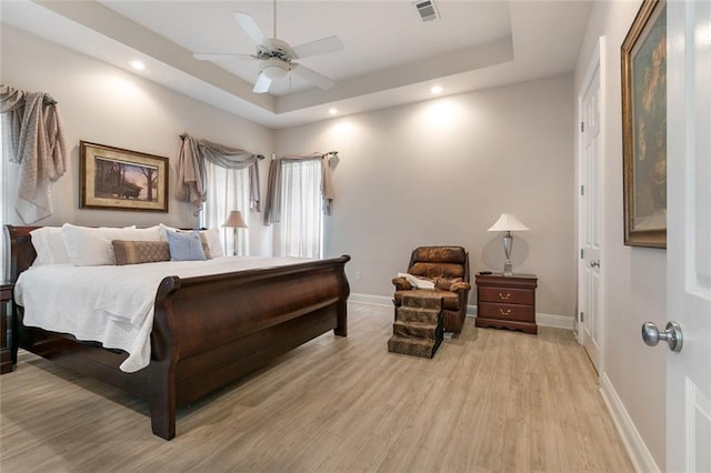 bedroom featuring light hardwood / wood-style floors, ceiling fan, and a tray ceiling